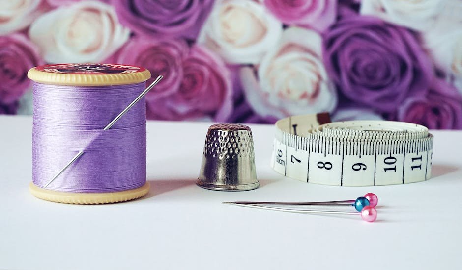 pexels-photo-1266139-1266139 A close-up of sewing tools including lilac thread, a thimble, tape measure, and colorful pins with a rose backdrop.